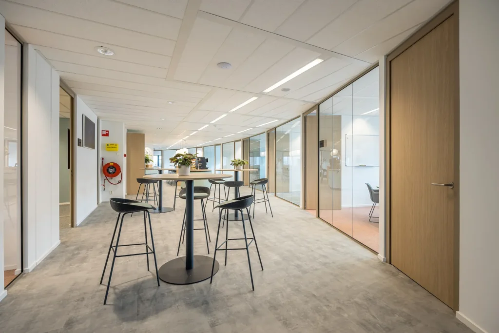 Moderne ontmoetingsruimte met hoge tafels en krukken in Zorggroep Haarlemmermeer.