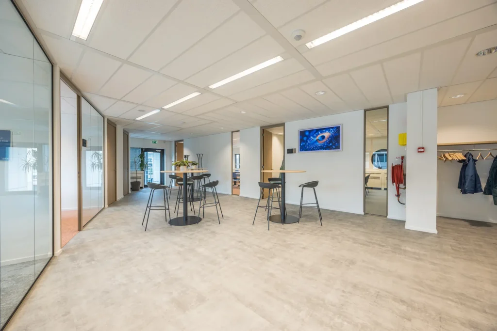 Moderne kantoorruimte van Zorggroep Haarlemmermeer met glazen wanden en hoge tafels.