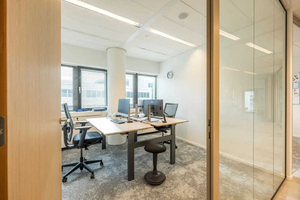 Een modern kantoor met twee werkplekken, computers en stoelen bij Zorggroep Haarlemmermeer.