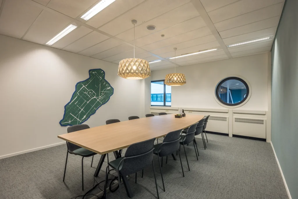Vergaderruimte van Zorggroep Haarlemmermeer met lange tafel, moderne hanglampen en een wanddecoratie van een plattegrond.