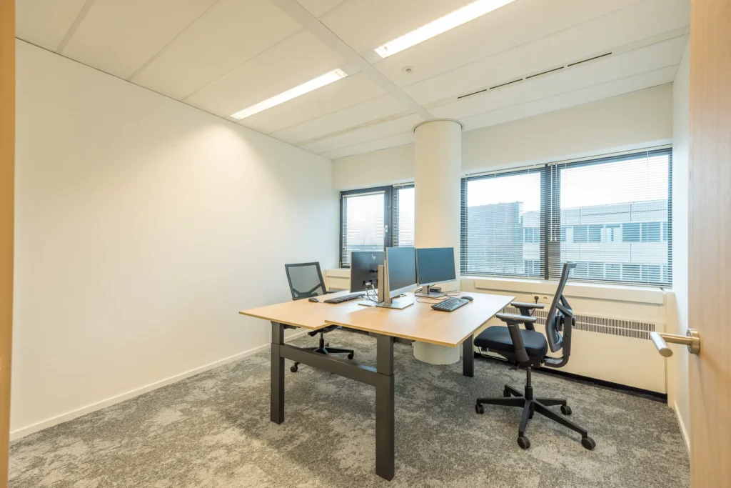 Een moderne, lichte kantoorruimte van de Zorggroep Haarlemmermeer met twee bureaustoelen en computerschermen.