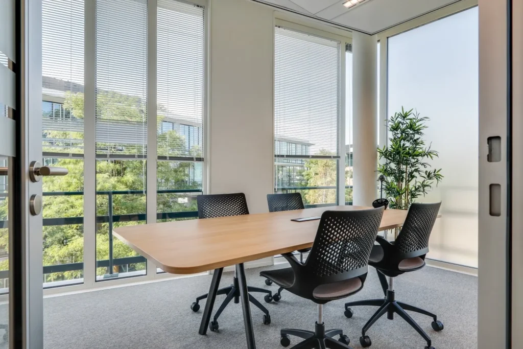 Een moderne vergaderruimte met designstoelen, veel natuurlijk licht en uitzicht op groene omgeving.