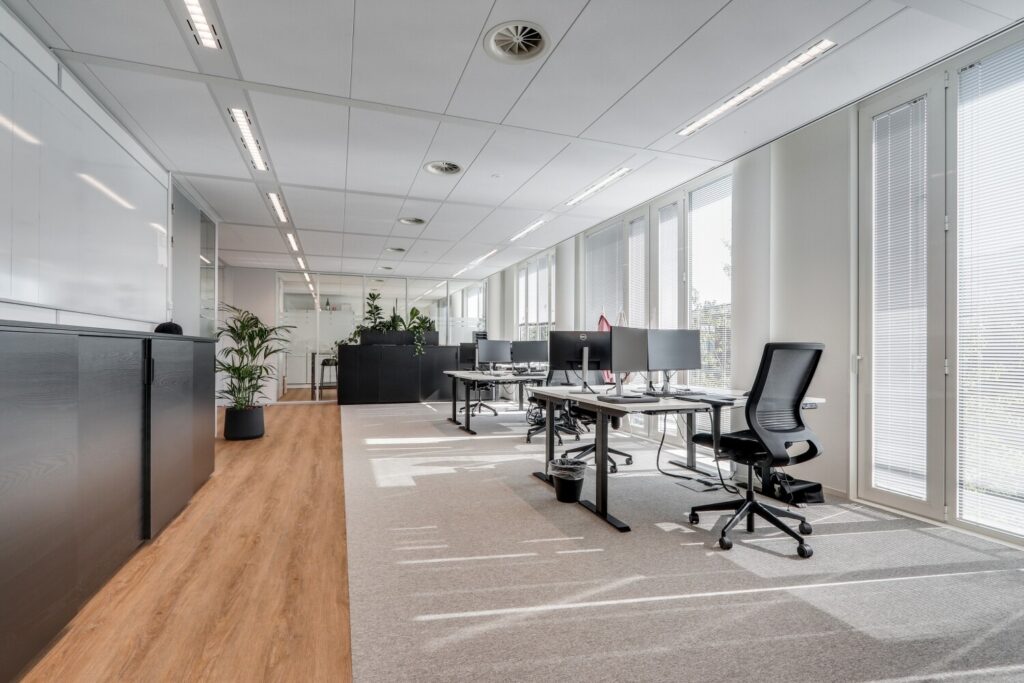 Een moderne, lichte kantoorruimte met werkplekken, planten en grote ramen bij Decuserstraat 89.