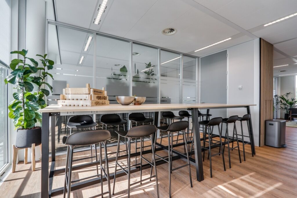 Moderne vergaderruimte met houten tafel, zwarte barkrukken en veel natuurlijk licht.