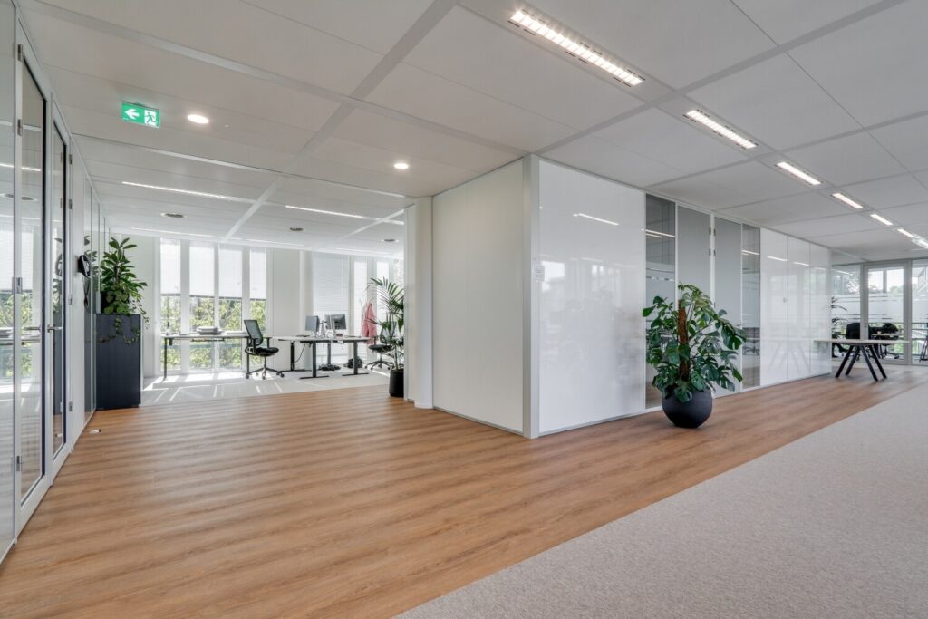 Moderne kantoorruimte met houten vloeren, glazen wanden en veel natuurlijke lichtinval.