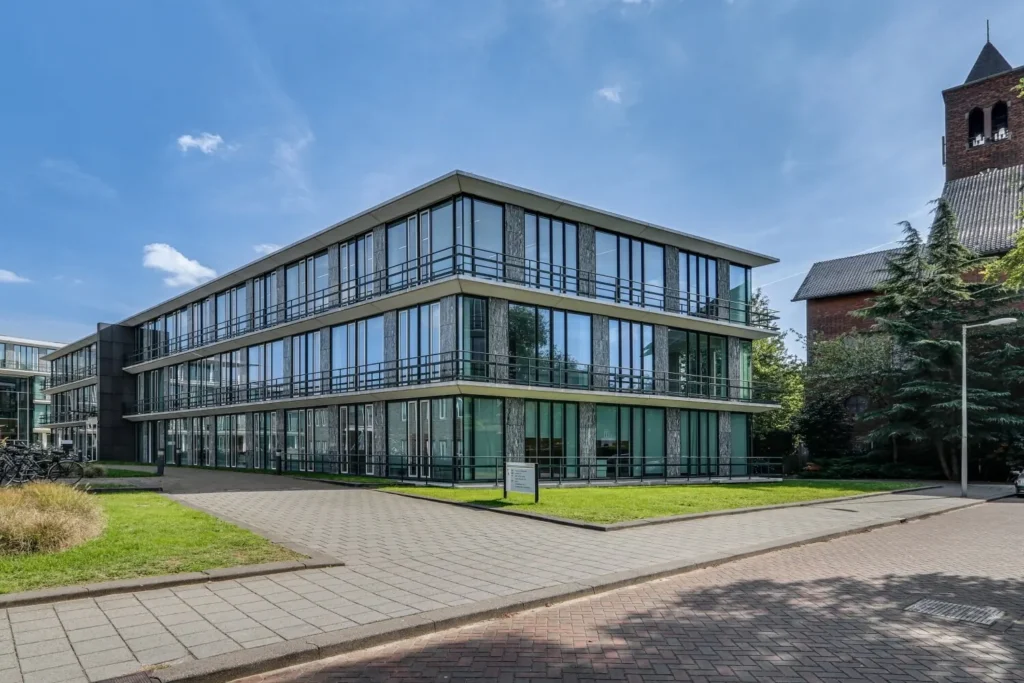 Modern kantoorgebouw met grote ramen aan de Decuserstraat, naast een klassieke kerk.