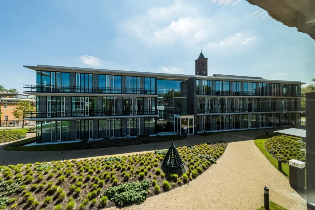 Modern kantoorgebouw aan de Decuserstraat 85-22 met een verzorgde tuin en klokketoren op de achtergrond.