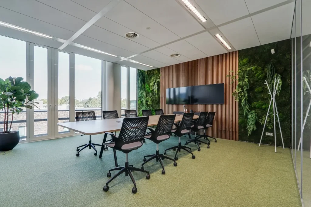Moderne vergaderruimte met grote ramen, een houten wand en groene plantendecoratie.