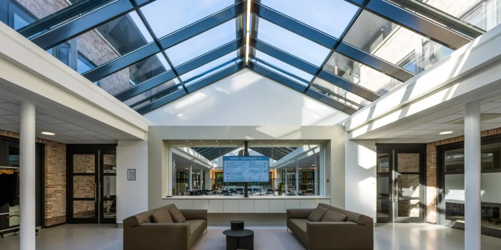 Een moderne, lichte ontvangsthal met glazen dak en comfortabele zithoek bij Elspeterweg 22-24 in Nunspeet.