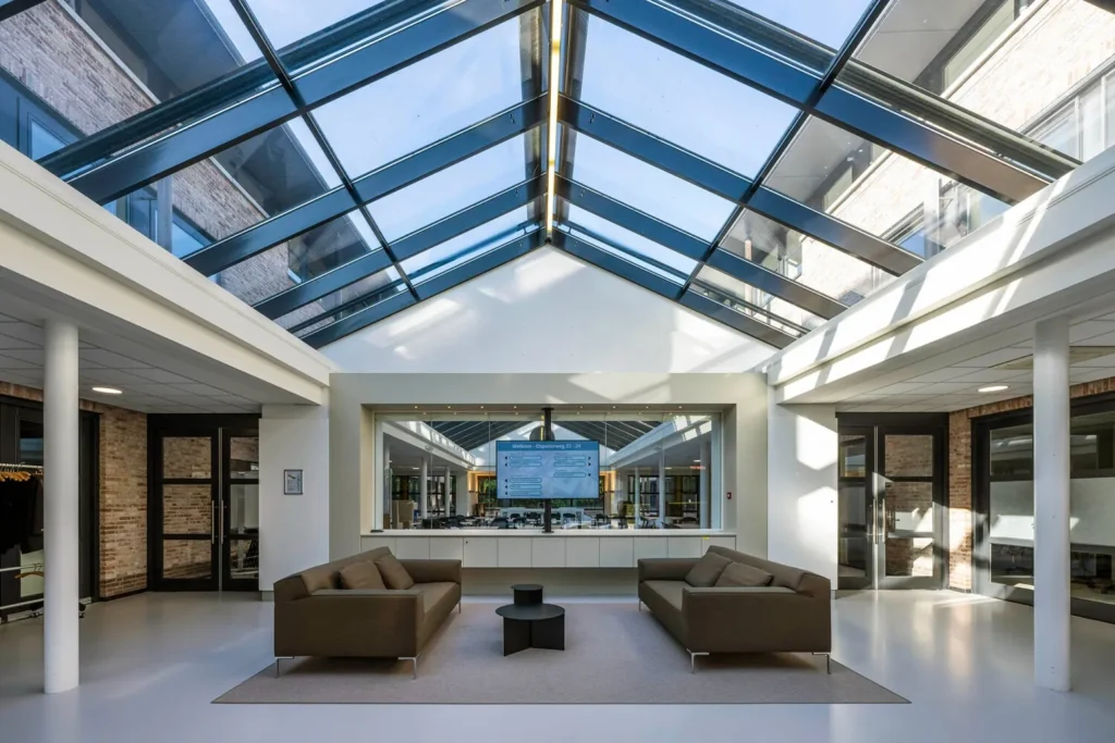 Open en lichte ontvangstruimte met glazen dak, moderne meubels en een centraal geplaatste informatiebalie aan de Elspeterweg 22-5.