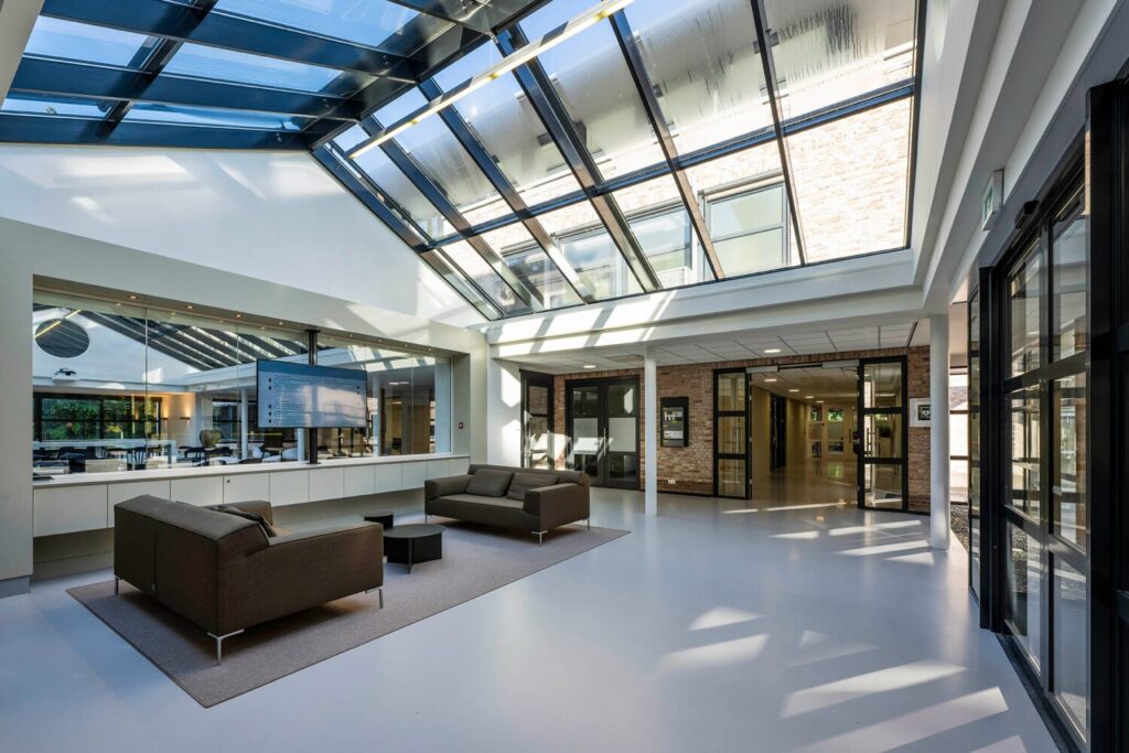 Moderne en lichte ontvangstruimte met glazen dak, comfortabele zitbanken en een groot scherm aan de muur in een gebouw aan de Elspeterweg.