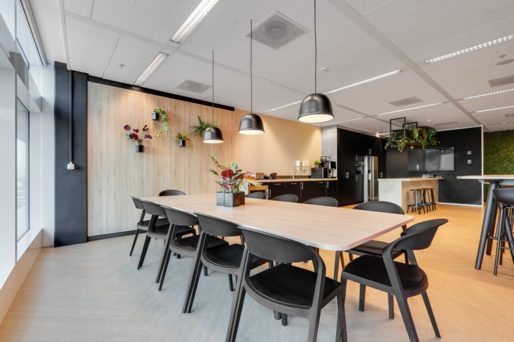 Een moderne kantoorruimte met een vergadertafel, hangende planten en een hoek voor koffievoorzieningen.