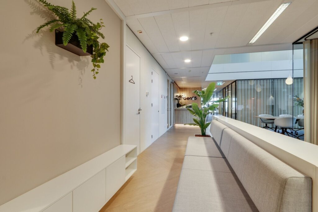 Moderne kantoorhal met witte muren, grijze zitbank en veel groen, met aan het einde het logo van Gen25.