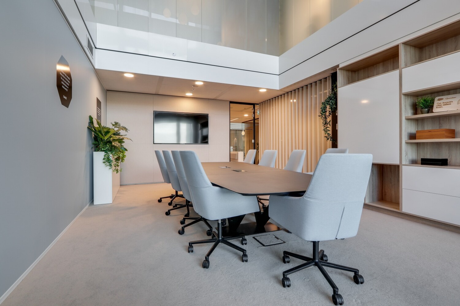 Moderne vergaderruimte met een grote tafel, comfortabele stoelen, een flatscreen-tv en decoratieve planten aan de Gustav Mahlerlaan.