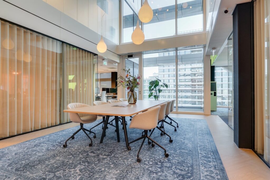 Een moderne vergaderruimte met een lange tafel, comfortabele stoelen en grote ramen met uitzicht op de stad, in Gustav Mahler 7.