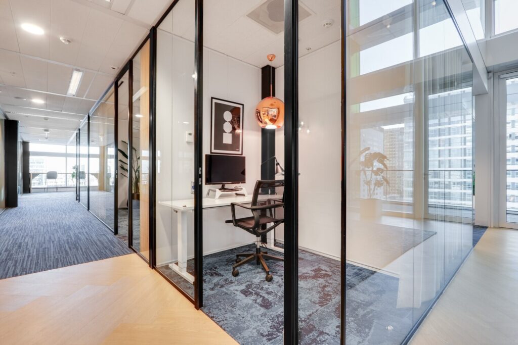 Moderne kantoorruimte met glazen wanden, ingericht met een bureau, stoel en computer, in het Gustav Mahler gebouw.