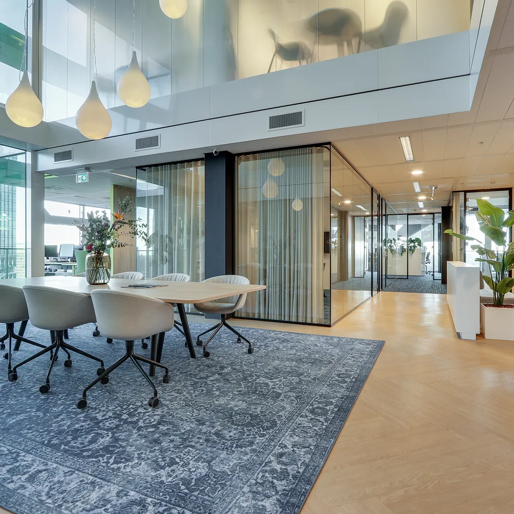 Modern ingerichte kantoorruimte met glazen wanden, een groot tapijt en een vergadertafel met stoelen.