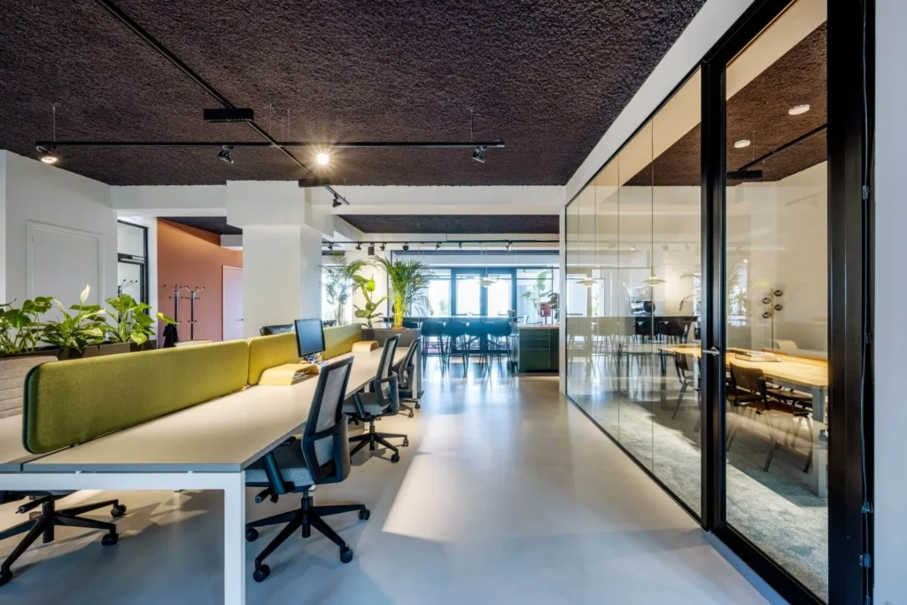 Modern en licht kantoorinterieur met glazen wanden, ergonomische bureaustoelen en decoratieve planten.