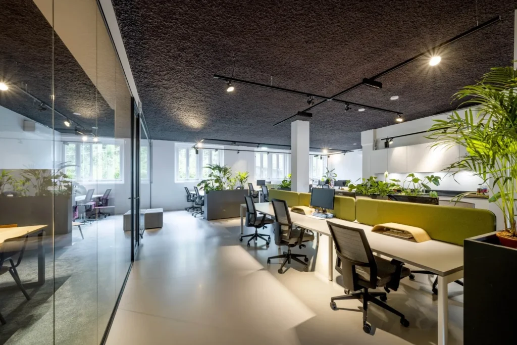 Moderne kantoorruimte met open werkplekken, veel natuurlijk licht en groene planten.