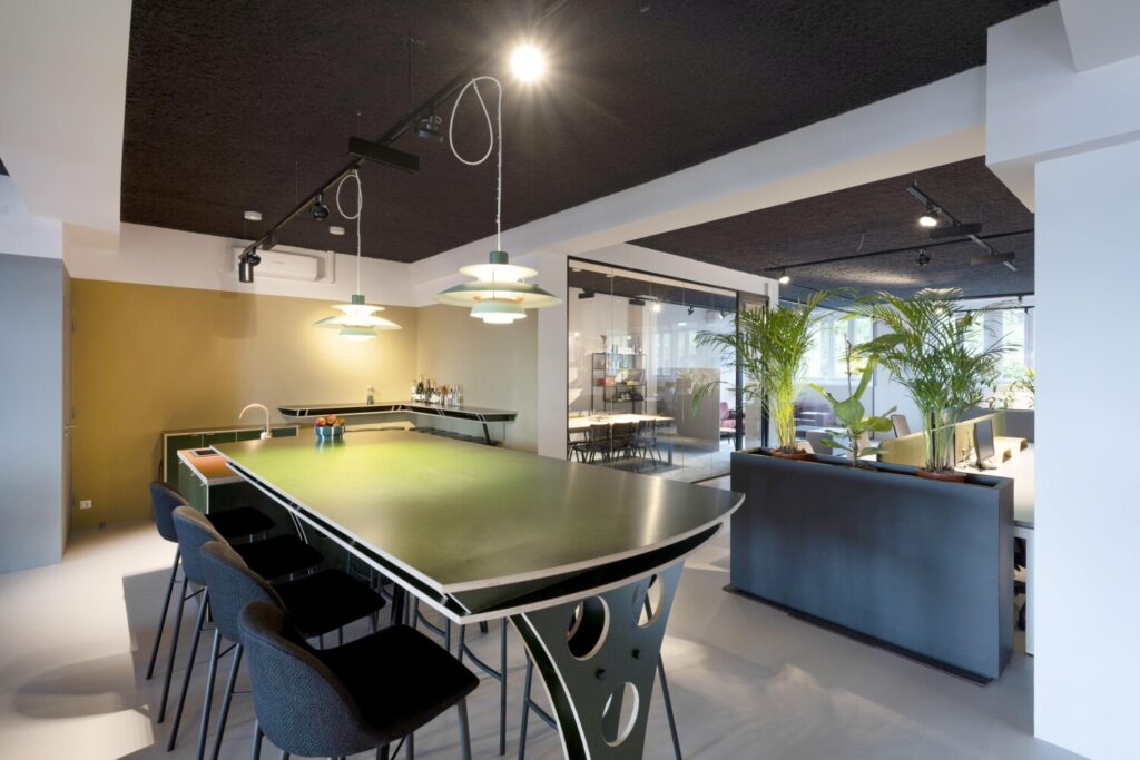 Een moderne kantoorruimte met een grote vergadertafel, stijlvolle hanglampen en groene planten.