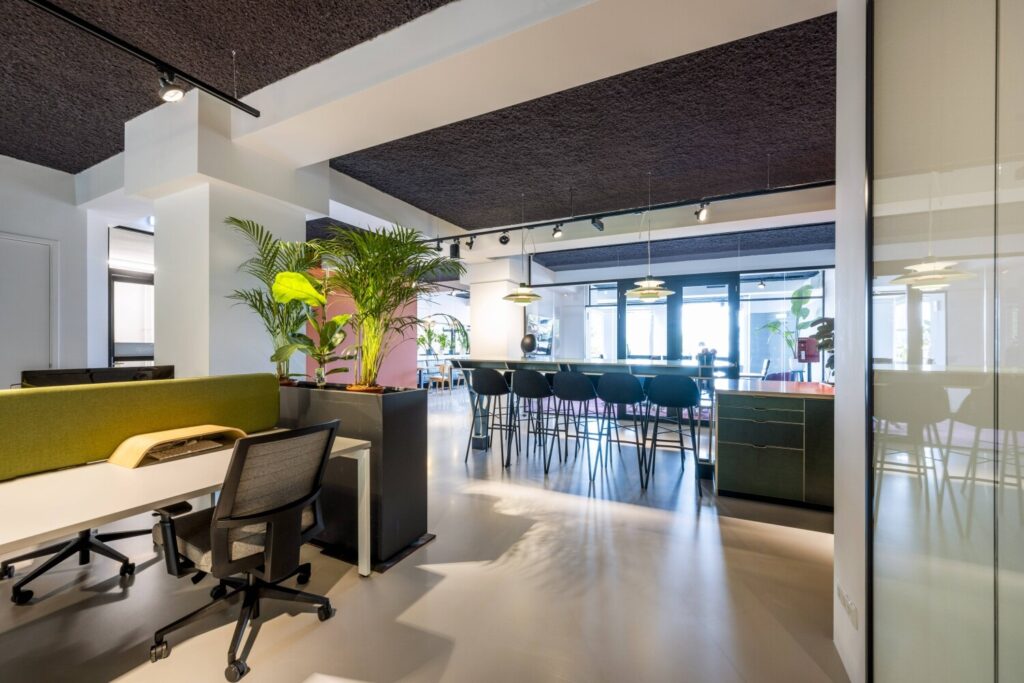 Moderne, ruime kantoorruimte met open werkplekken, groene planten en een lange tafel.