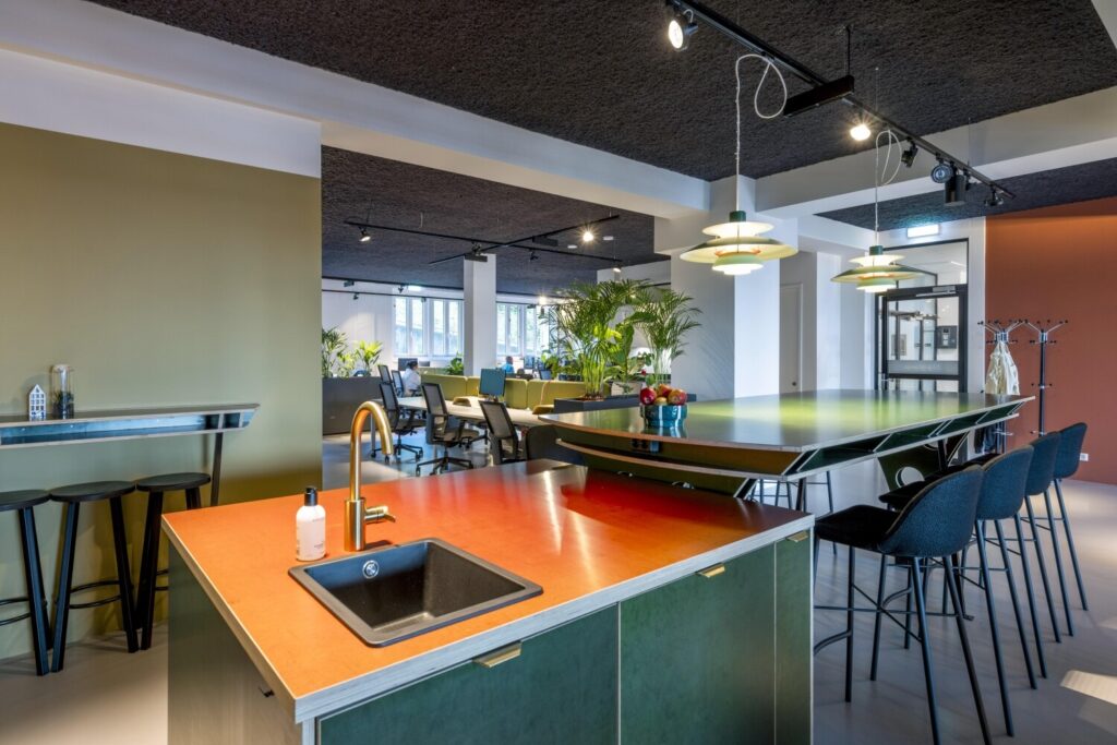 Moderne kantoorruimte met een open keukeneiland, groene accenten en stijlvolle zitplaatsen.