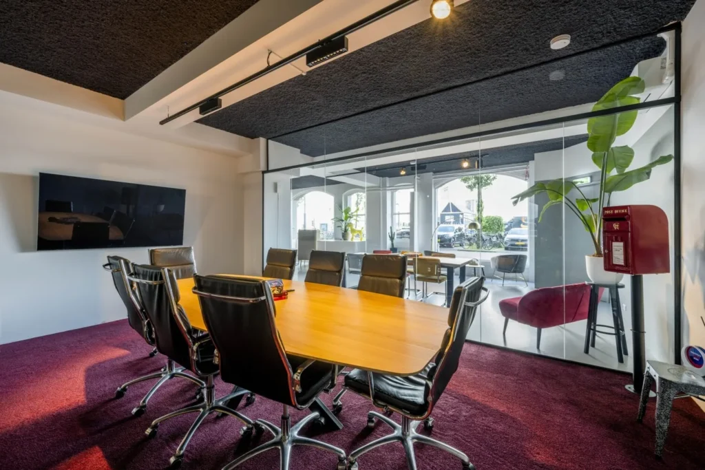 Moderne vergaderruimte met glazen wanden, een lange houten tafel en comfortabele zwarte stoelen.