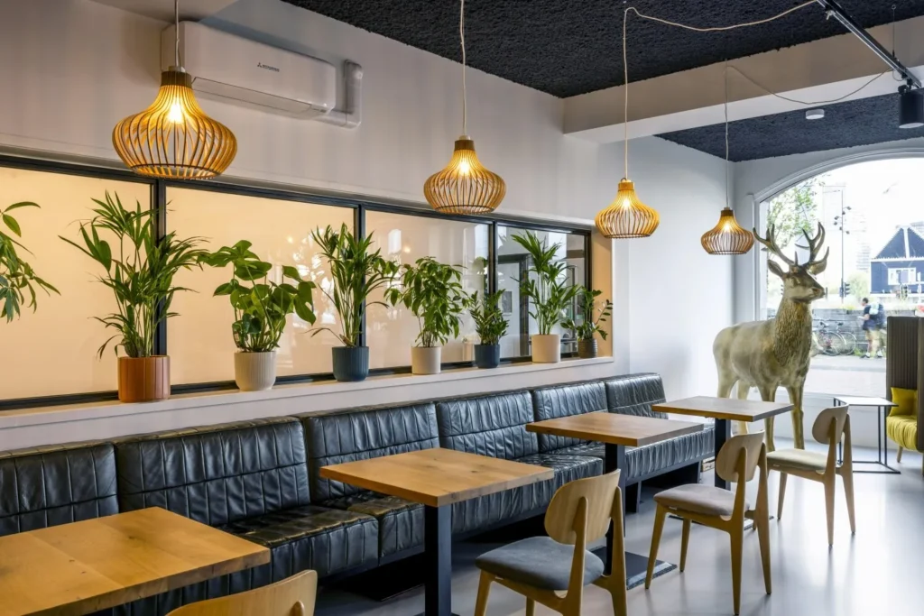 Een modern café-interieur met houten tafels, zwarte leren banken, hanglampen van hout en een grote hertensculptuur bij de deur.