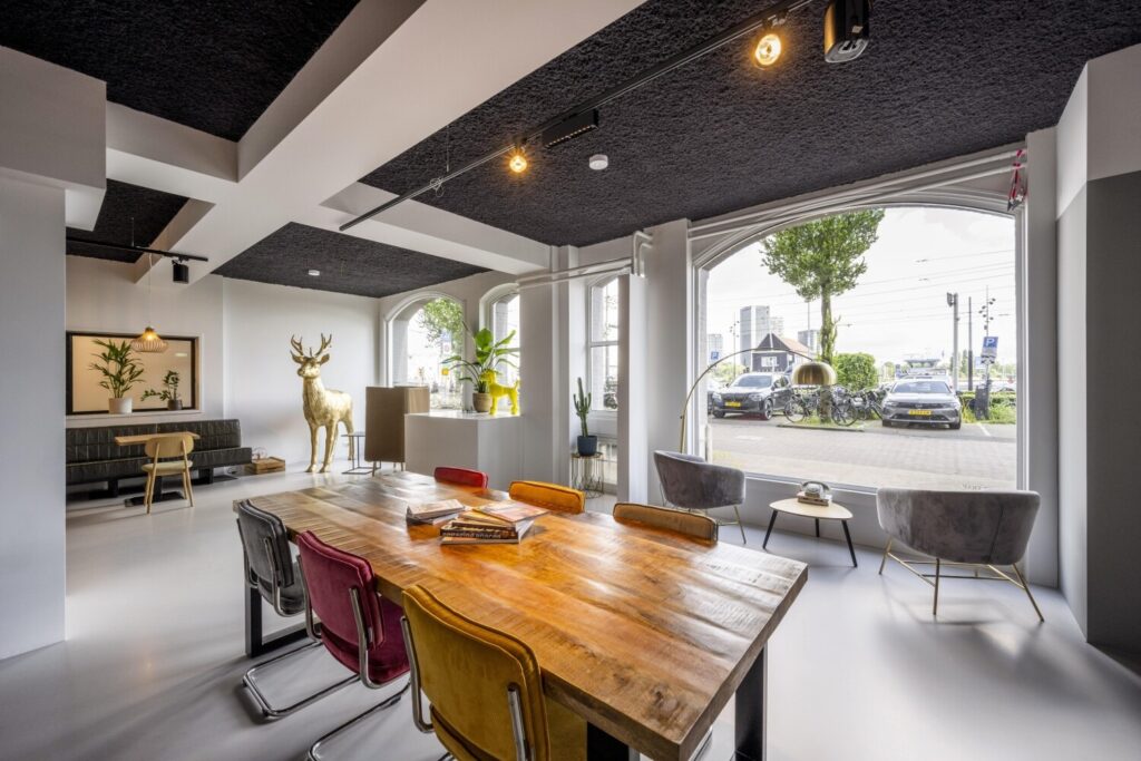 Moderne kantoorruimte met houten tafel, kleurrijke stoelen en groot raam met uitzicht op straat.