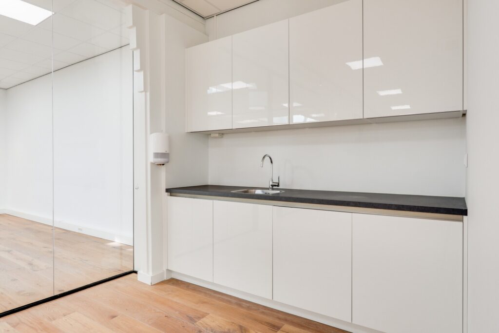 Moderne keuken met witte kasten en een donker aanrechtblad in een lichte kantooromgeving aan de Keizersgracht.