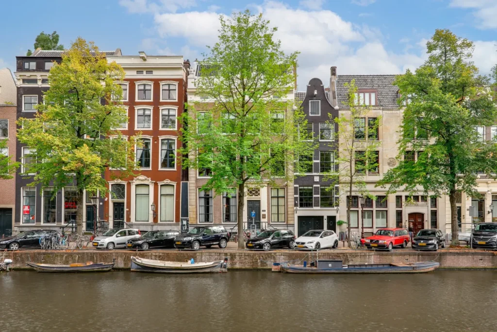 Gevels van statige grachtenpanden aan de Keizersgracht in Amsterdam met auto's en fietsen langs de kade.