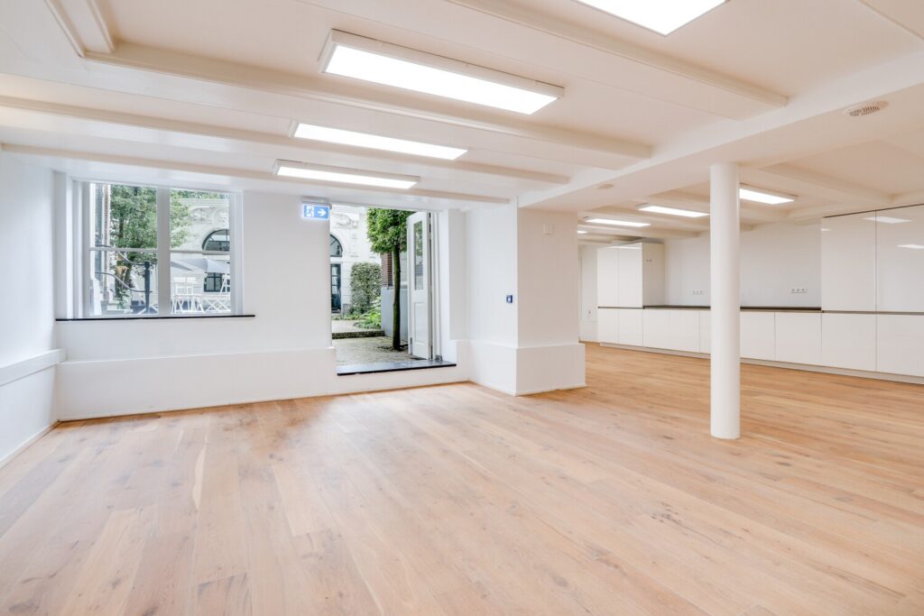 Lichte, moderne bedrijfsruimte met houten vloer en open toegang tot een buitenplaats aan de Keizersgracht.