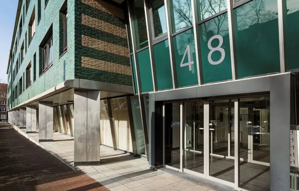 Entree van een modern gebouw met het nummer 48, met groene gevel en grote glazen deuren.