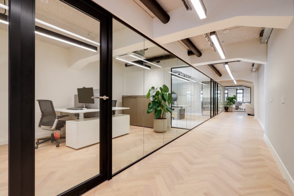 Moderne kantoorruimte met glazen wanden en houten visgraatvloer in een licht interieur.