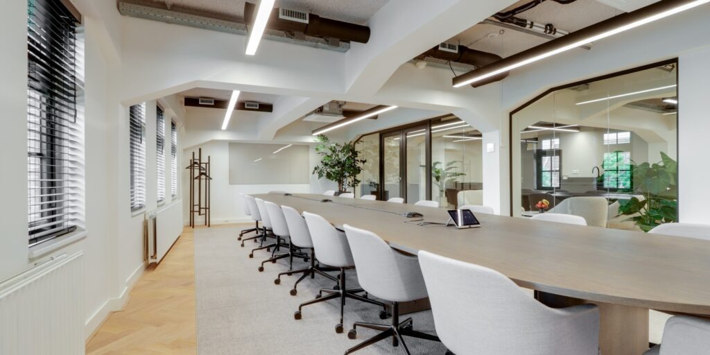 Moderne vergaderruimte met een lange tafel, omringd door comfortabele stoelen en veel natuurlijk licht.