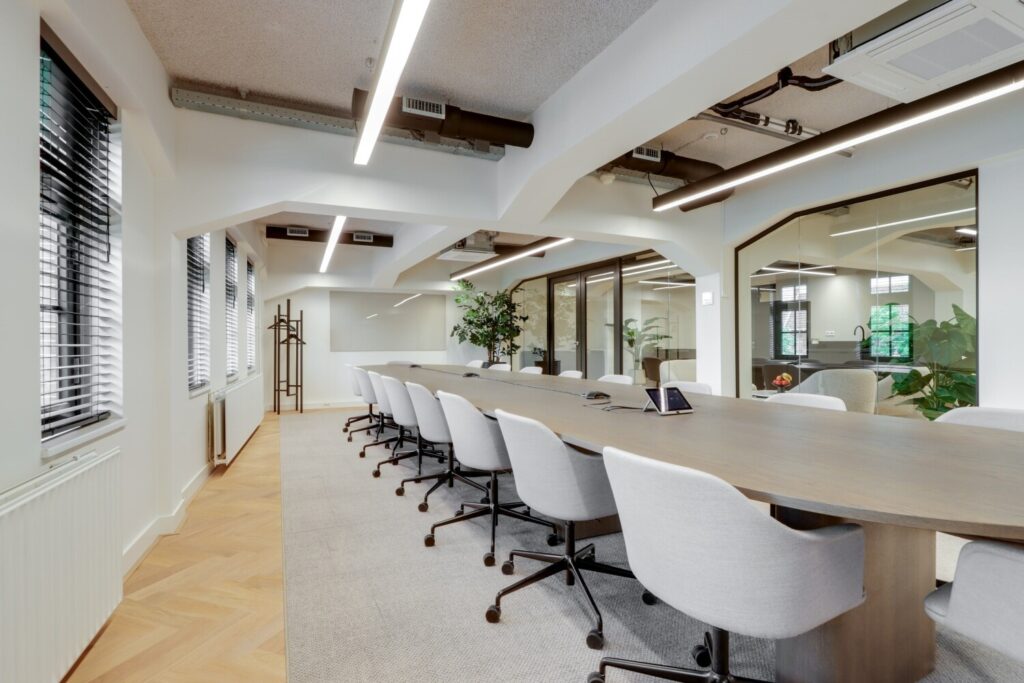 Moderne vergaderruimte met een lange houten tafel en comfortabele stoelen in een lichte kantooromgeving.