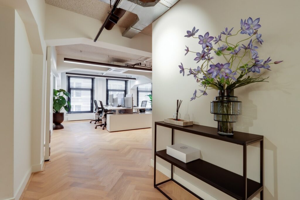 Moderne kantoorruimte met een strak bureau, ergonomische stoelen, en een decoratieve vaas met paarse bloemen op de voorgrond.