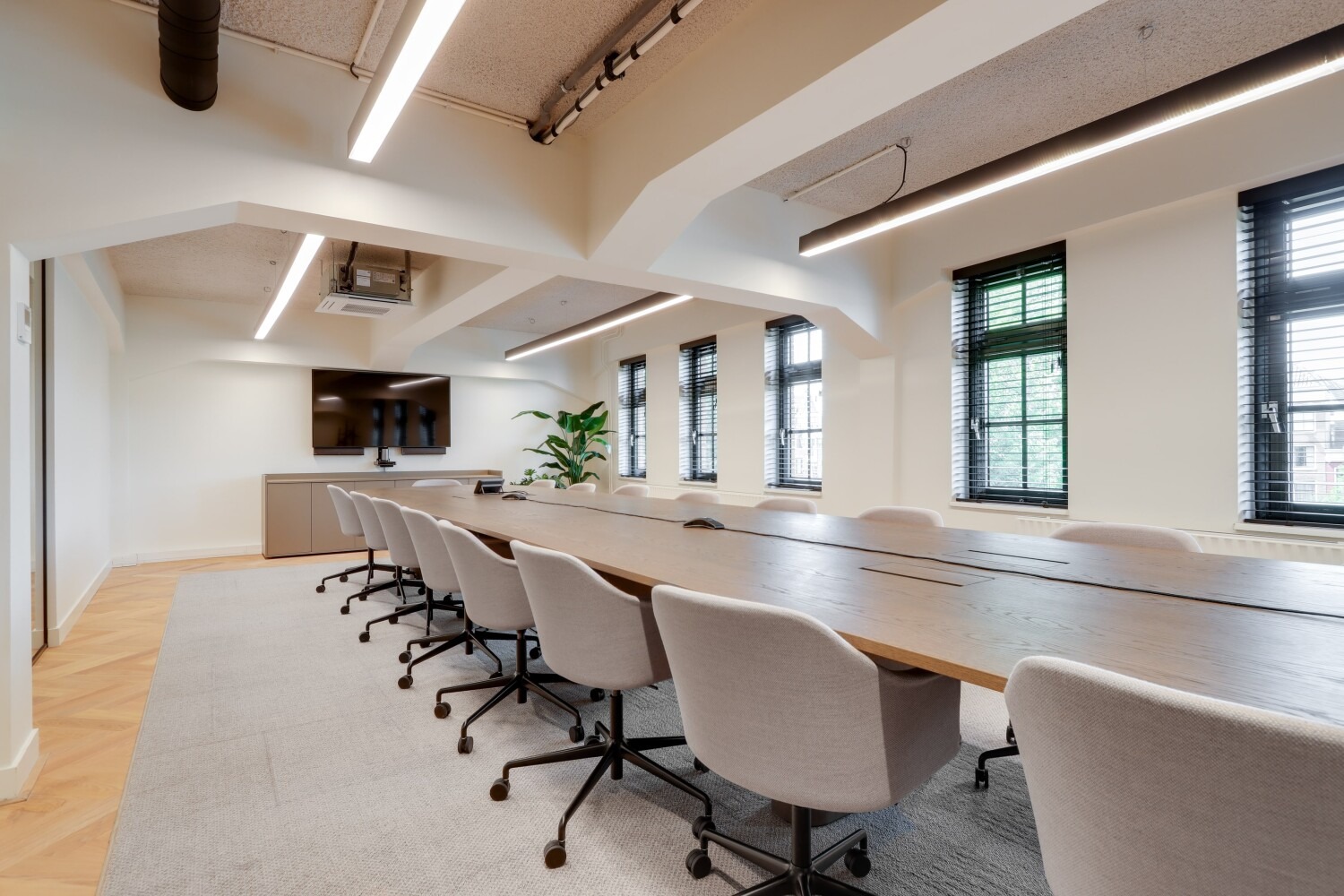 Vergaderruimte in modern kantoor met lange houten tafel, comfortabele stoelen en grote ramen.