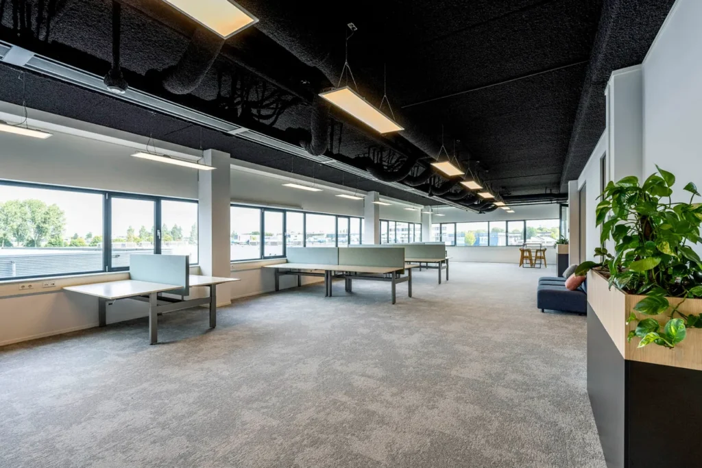 Moderne, lichte kantoorruimte op Transformatorweg 76 met bureaus en groene planten.