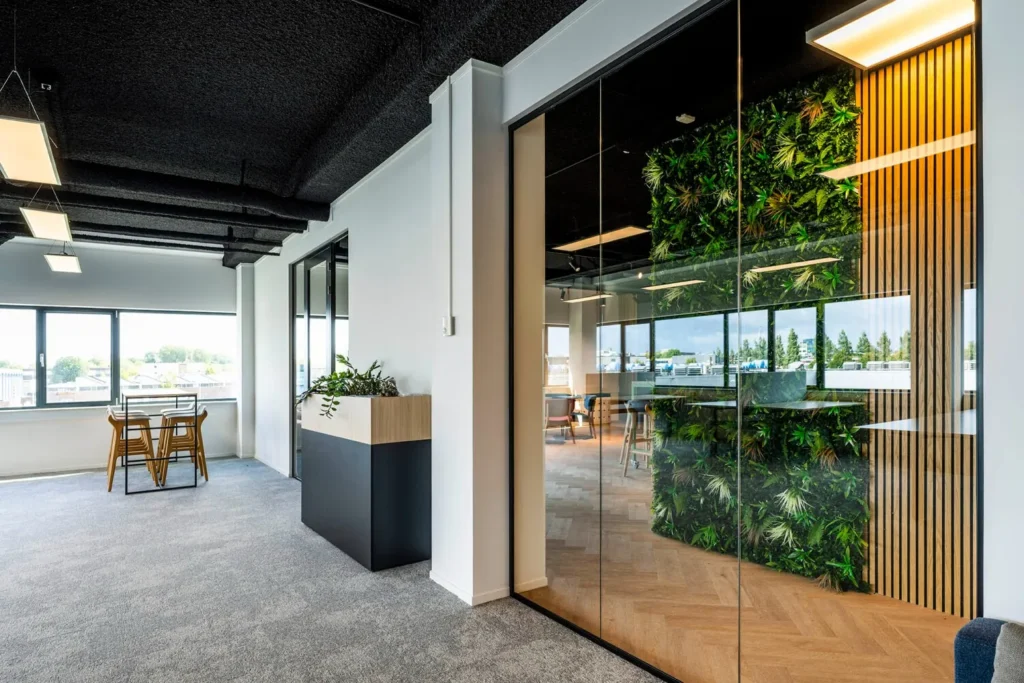 Modern kantoor met glazen wanden, houten meubels en een groene plantenwand op Transformatorweg 76.