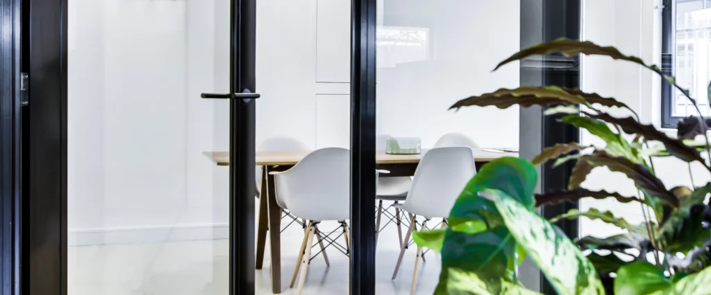 Moderne vergaderruimte met glazen deuren en witte stoelen, omgeven door groen.