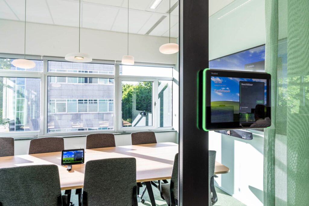 Moderne vergaderruimte in Winthontlaan 10 met digitale reserveringsschermen en een grote tafel omgeven door stoelen.