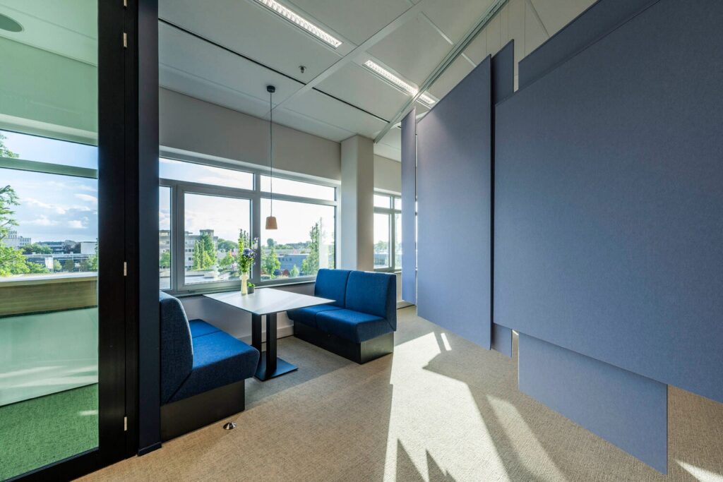 Moderne vergaderruimte met blauwe zitbanken, een tafel en akoestische panelen bij Winthontlaan 16, met uitzicht op de stad.