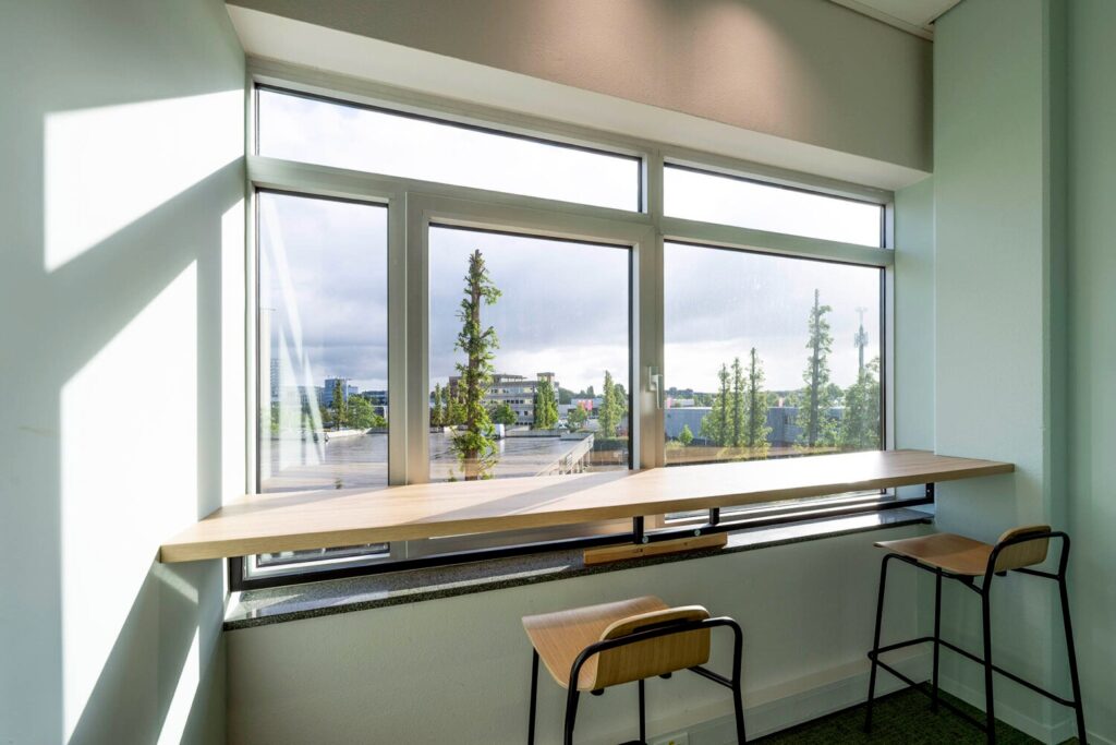 Lichte kantoorruimte op Winthontlaan 20 met een houten zitbank en uitzicht op bomen en gebouwen.